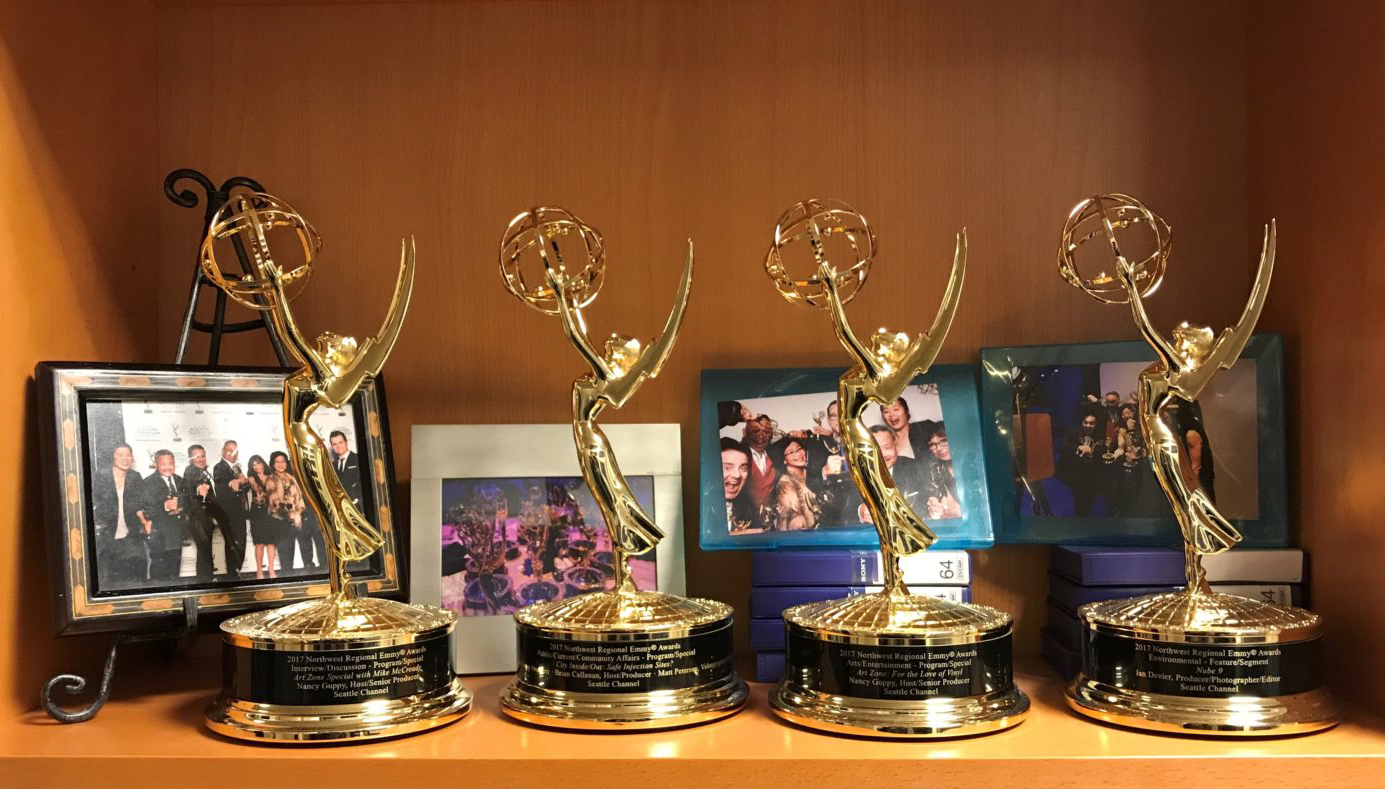 A bookshelf at the Seattle Channel studios holds four Emmy awards and framed photos of employees at past Emmy ceremonies.